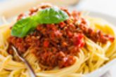 Sauce Bolognese Bowl of delicious Italian spaghetti Bolognese topped with a rich meat and tomato sauce and sprinkled with grated parmesan cheese with a wedge behind